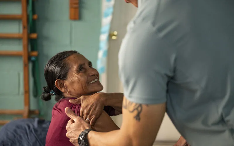 Juana Vasquez Gonzalez, a Comayagua local, smiles as U.S. Army Reserve Maj. Collier Amundson, Army Forces Medical Detachment Chief of Rehabilitation, checks for shoulder tightness at Centro de Rehabilitacion Integral de Comayagua, Comayagua, Honduras, Sept. 17, 2025. Amundson sees four to seven patients weekly to provide physical therapy and further develop his skills as a physical therapist. (U.S. Air Force photo by Staff Sgt. Sadie Colbert)