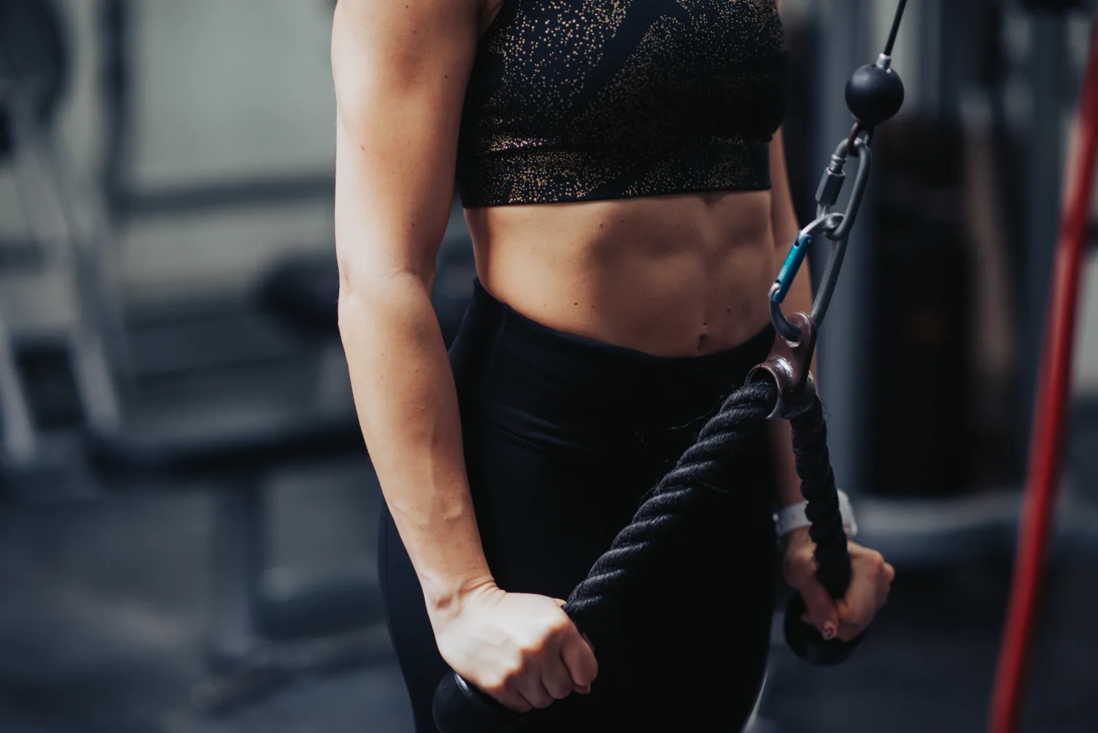 A fit woman performs an upper body exercise using a cable machine in a gym. She focuses on strength training, showcasing toned arms and abs.