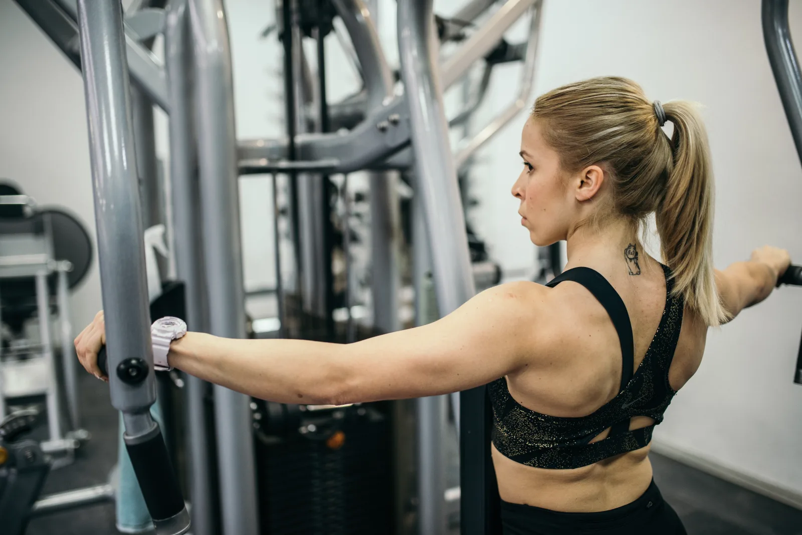 A woman is engaged in a strength training workout in a gym, focusing on her upper body. The setting showcases gym equipment and a bright, energetic atmosphere.