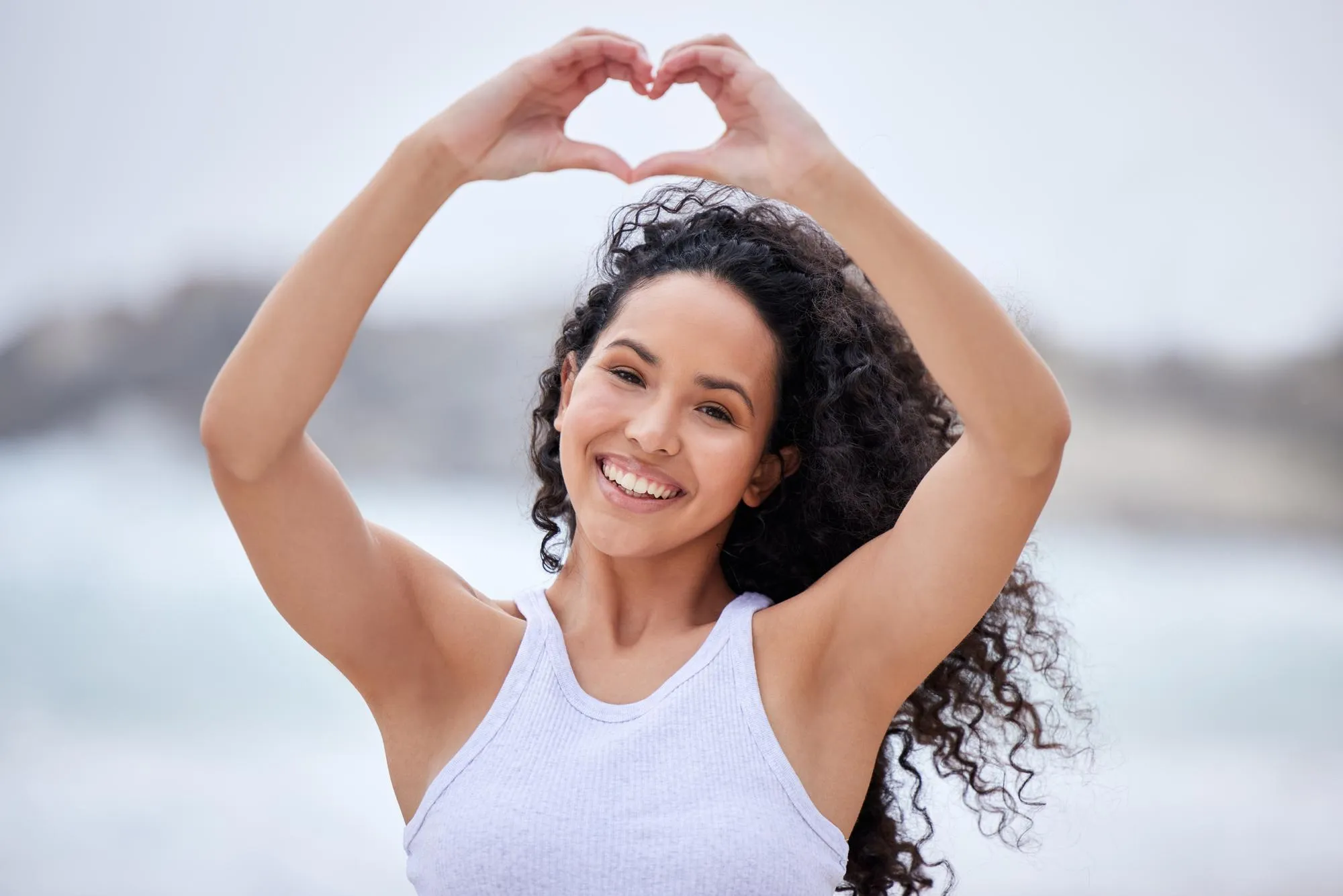 Beach portrait and woman with hands in heart for travel outdoor adventure and love of ocean Happy female person and smile with emoji on vacation for holiday support or weekend trip in California