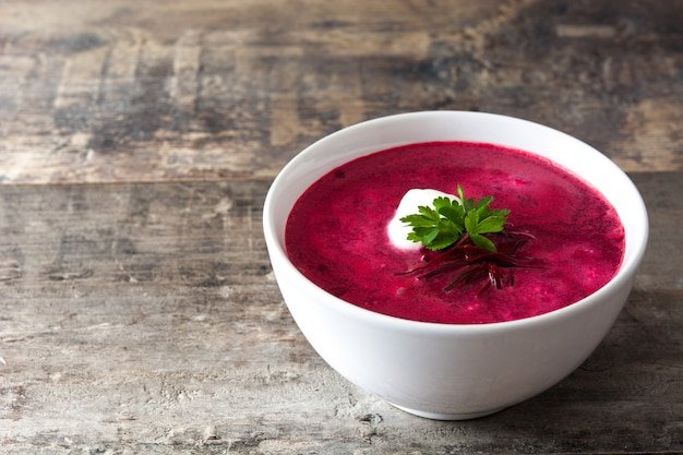 Beet soup in white bowl on wooden table copy space