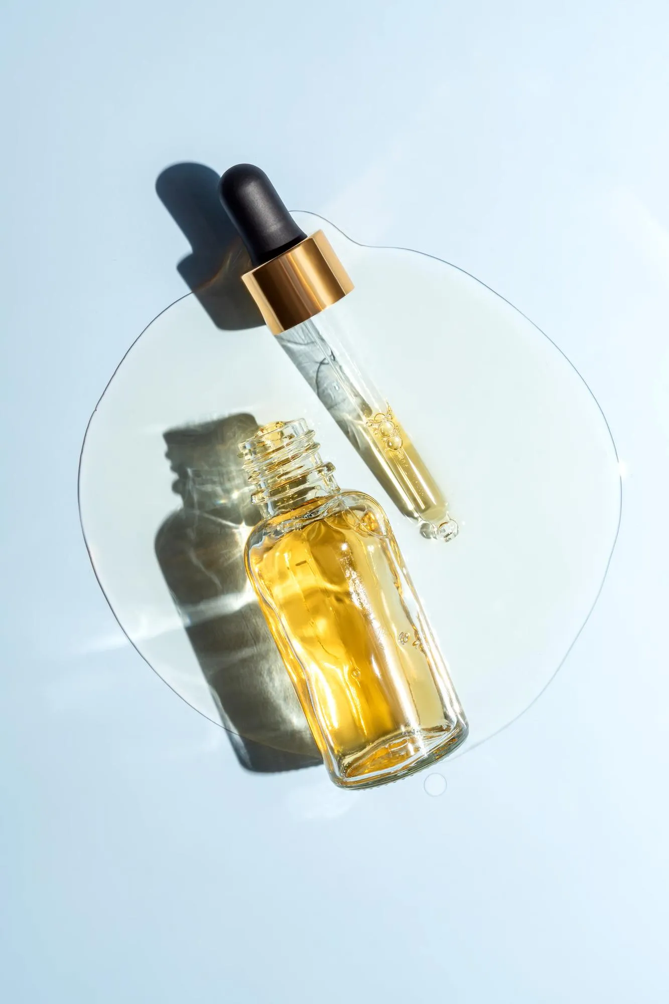 Face beauty oil spilled out of the dropper bottle on blue background Concept of skin care serum Unbranded product packaging