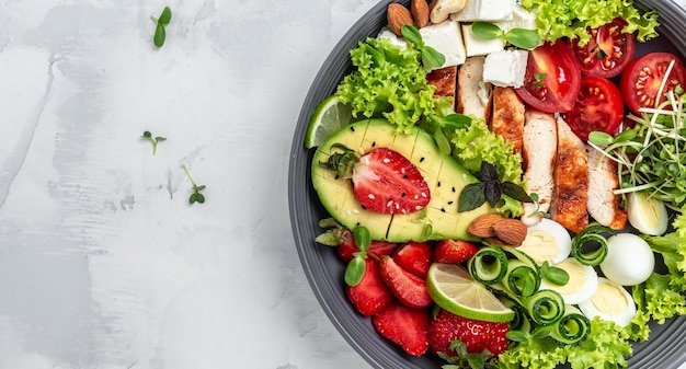 Healthy dinner. Buddha bowl lunch with grilled chicken and avocado, feta cheese, quail eggs, strawberries, nuts and lettuce. Healthy food trend. Top view.