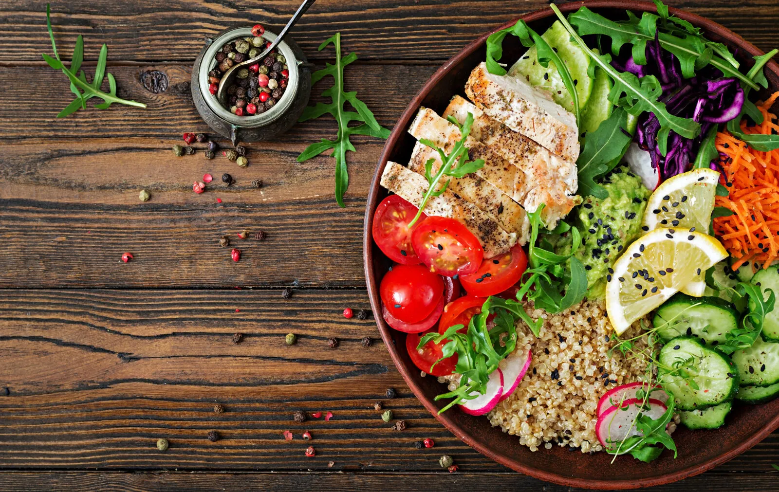 Healthy dinner. Buddha bowl lunch with grilled chicken and quinoa, tomato, guacamole, carrot, red cabbage, cucumber and arugula on wooden table. Flat lay. Top view