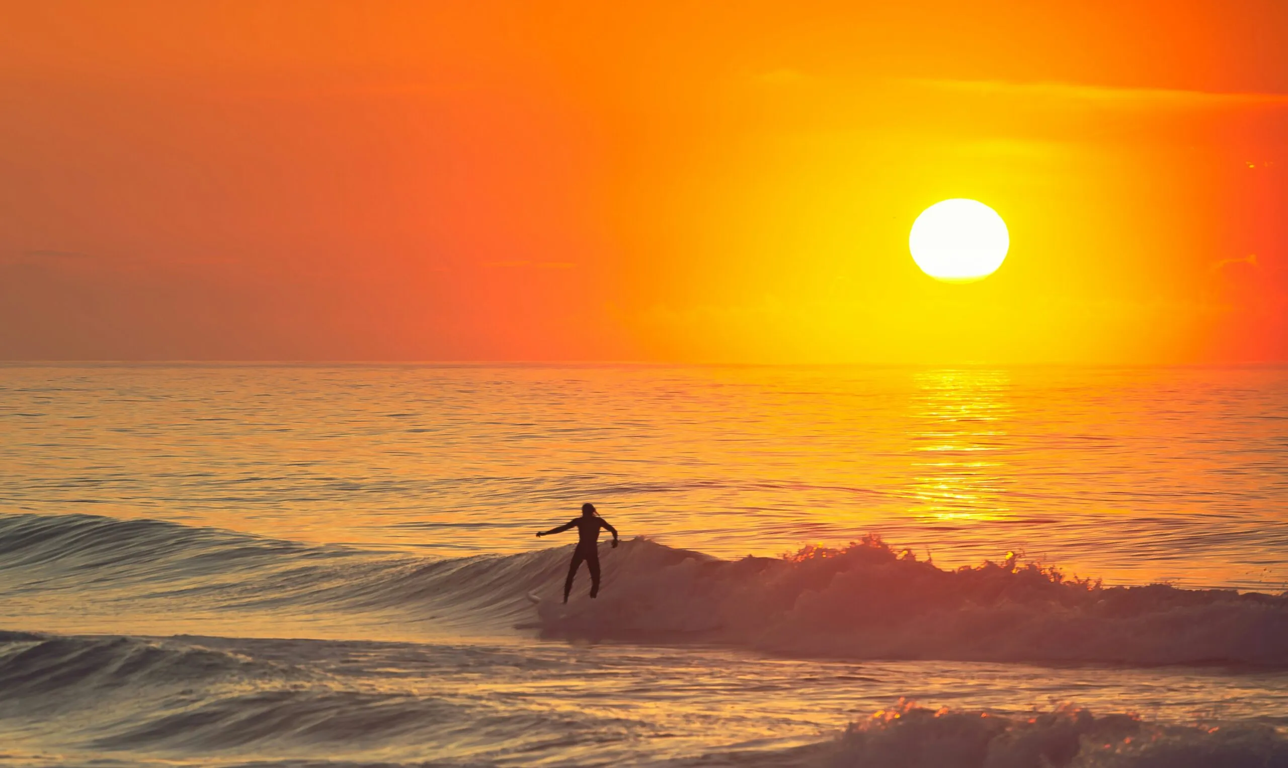 Surfer riding a wave during a vibrant orange sunset