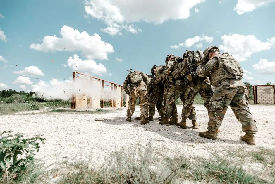 Group of soldiers in military uniforms performing a training exercise outdoors with explosive simulation.