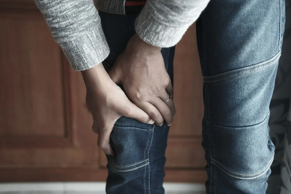 A person holds their knee in denim jeans, showing a sense of tension.