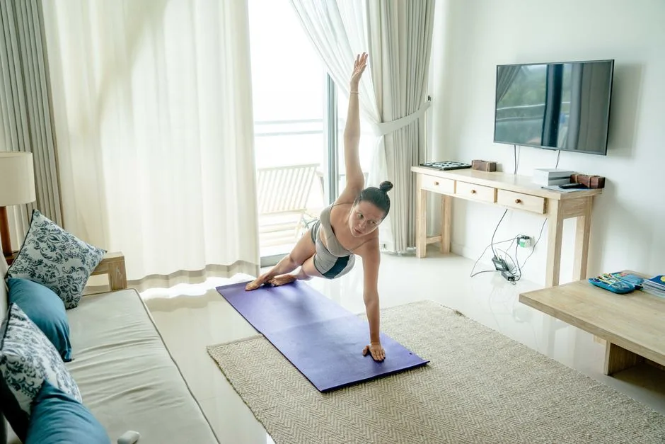 A woman practices yoga in a bright living room, performing a side plank on a mat.