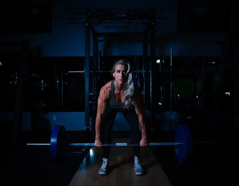 A fit woman lifting a barbell in a dimly lit gym, showcasing strength and determination.