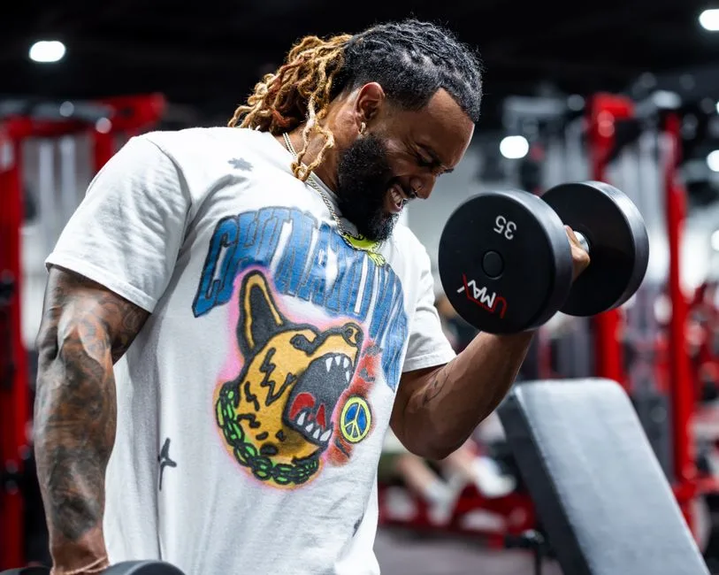 A determined man with tattoos lifting dumbbells in a gym setting.