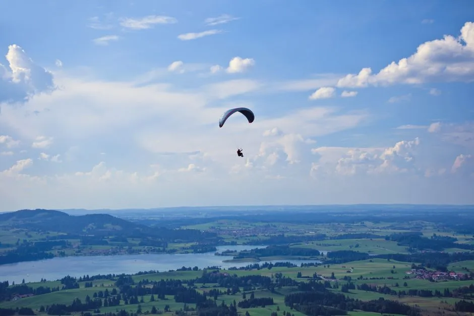 A paraglider soars above lush landscapes and lakes in Buchenberg, Bavaria.