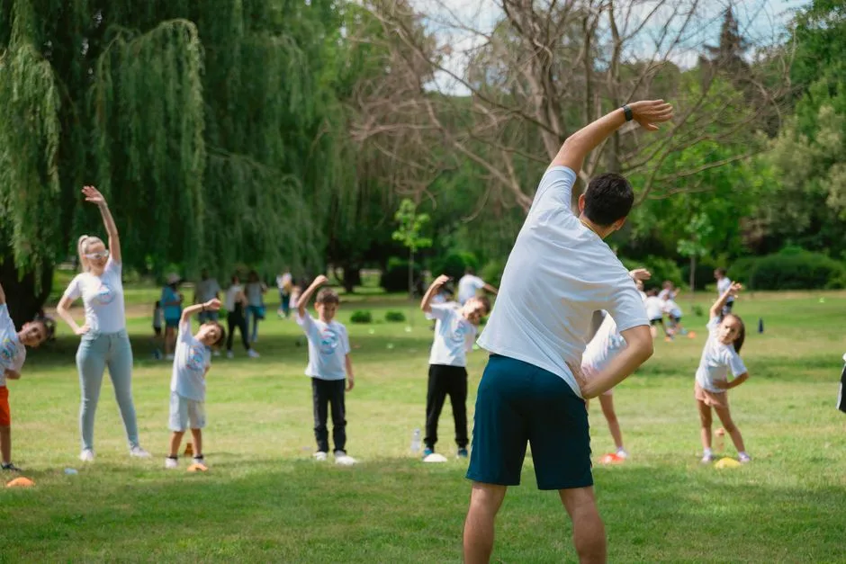 Children and instructors stretching in a park during a summer physical education class.