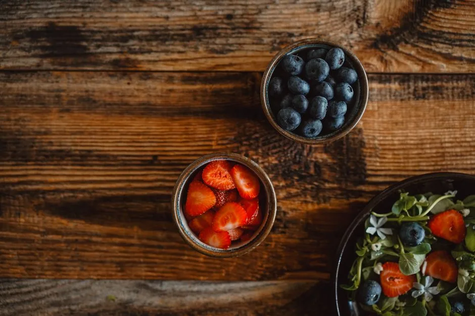 Top view of fresh strawberries, blueberries, and a salad displayed on a rustic wooden table.