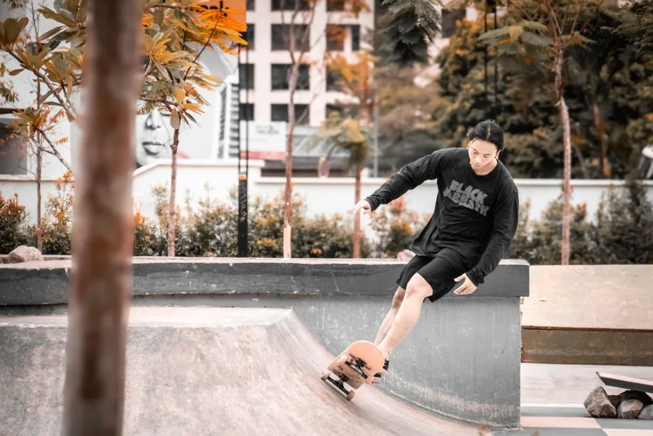 Young adult skateboarder performing a trick in an outdoor urban skate park surrounded by trees.