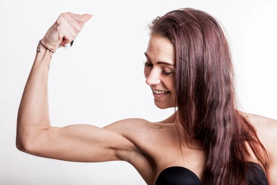 A confident woman flexing her bicep, showcasing strength and fitness in a studio setting.