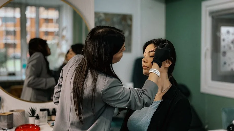 A makeup artist professionally applies eyebrow makeup to a female client in a salon.