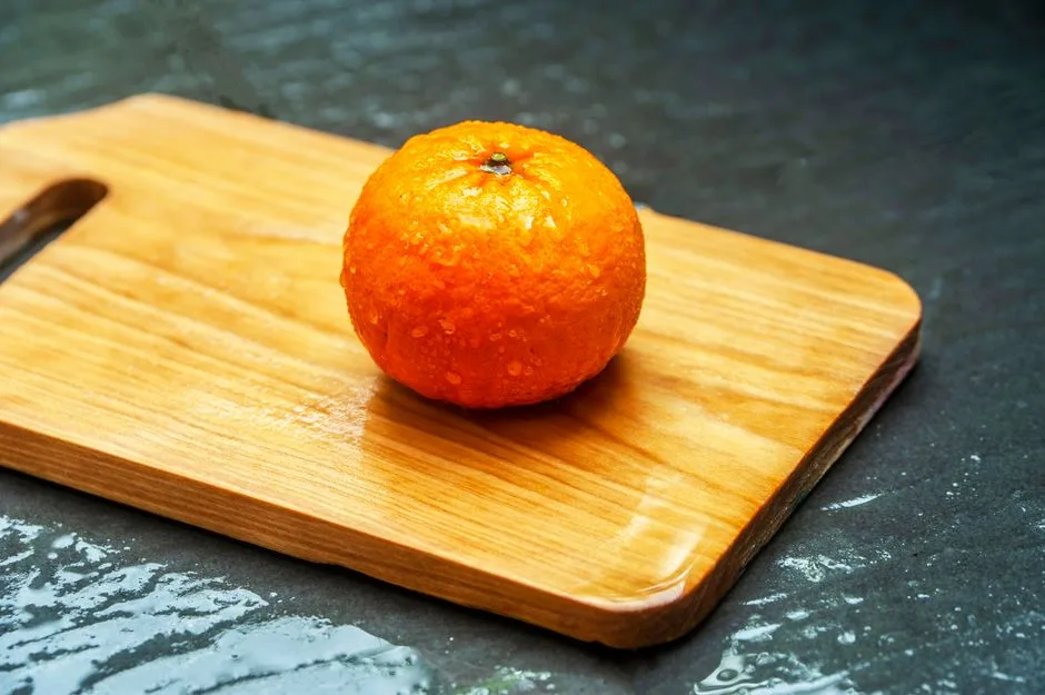 Single orange with water droplets on a wooden cutting board, showcasing freshness.
