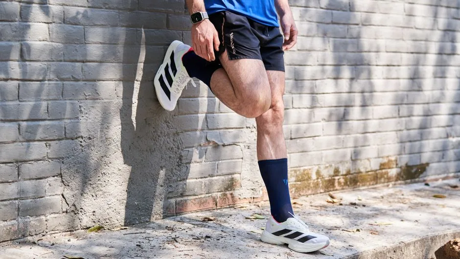 Man in athletic wear stretching his leg against a brick wall.