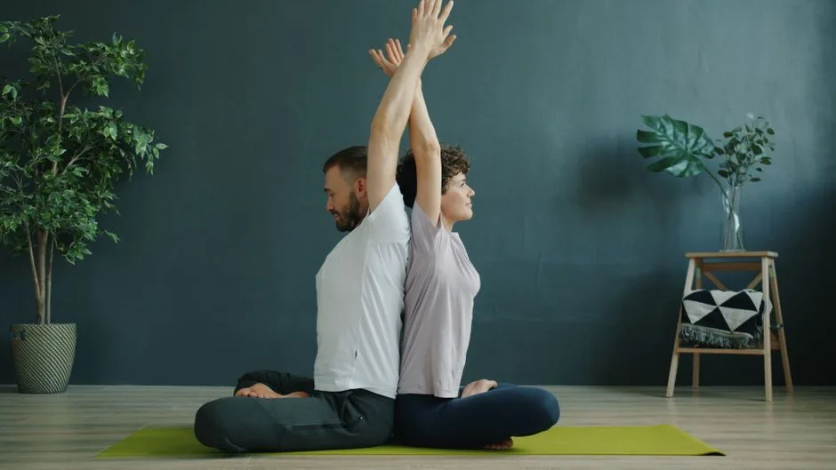 Two adults performing seated yoga poses on a mat indoors.
