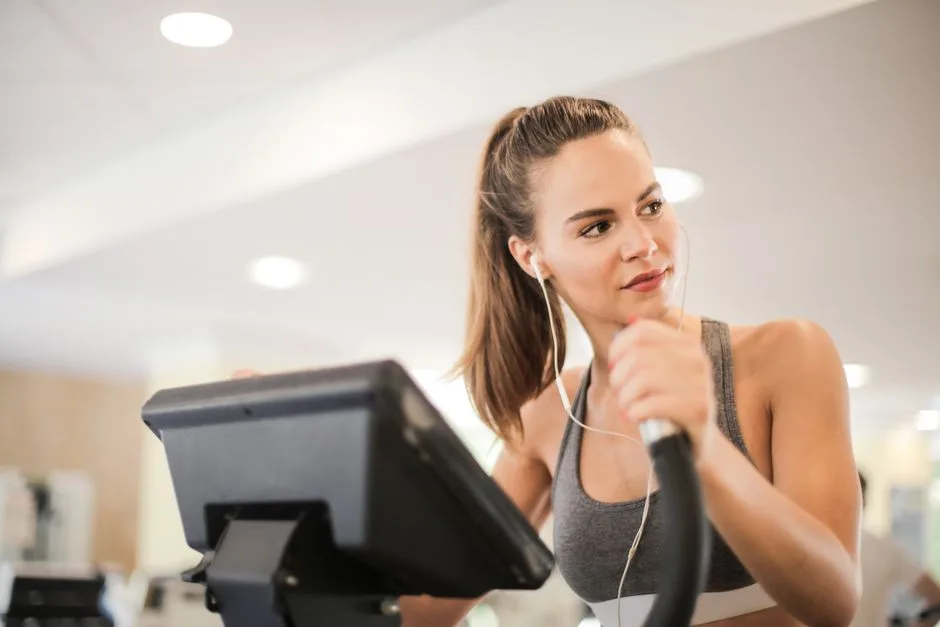 Fit woman working out on an elliptical machine indoors, wearing headphones and a sports bra.