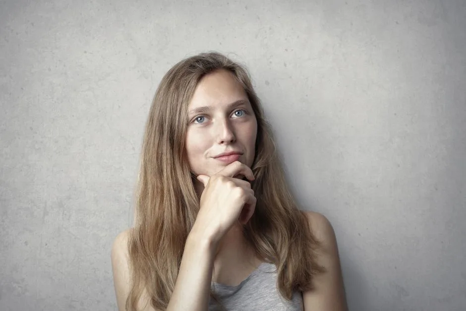 A thoughtful woman contemplates life in a simple portrait with a gray background.