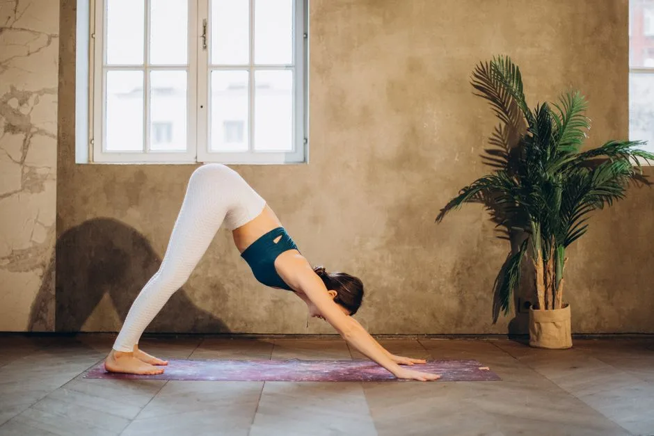 Woman performs downward dog yoga pose indoors near a window, promoting mindfulness and wellness.