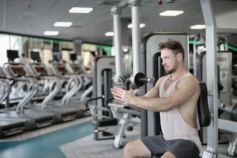 Serious strong male athlete in casual sportswear sitting on pec deck machine and performing exercise bringing hands together and looking forward in modern fitness center