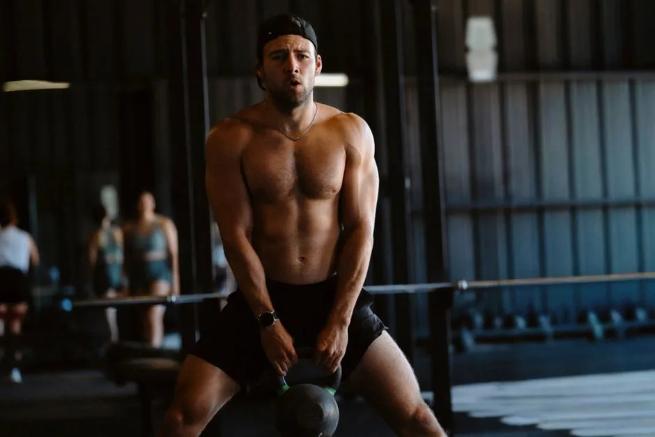 Muscular man doing kettlebell exercise in a gym setting. Fitness and strength training concept.
