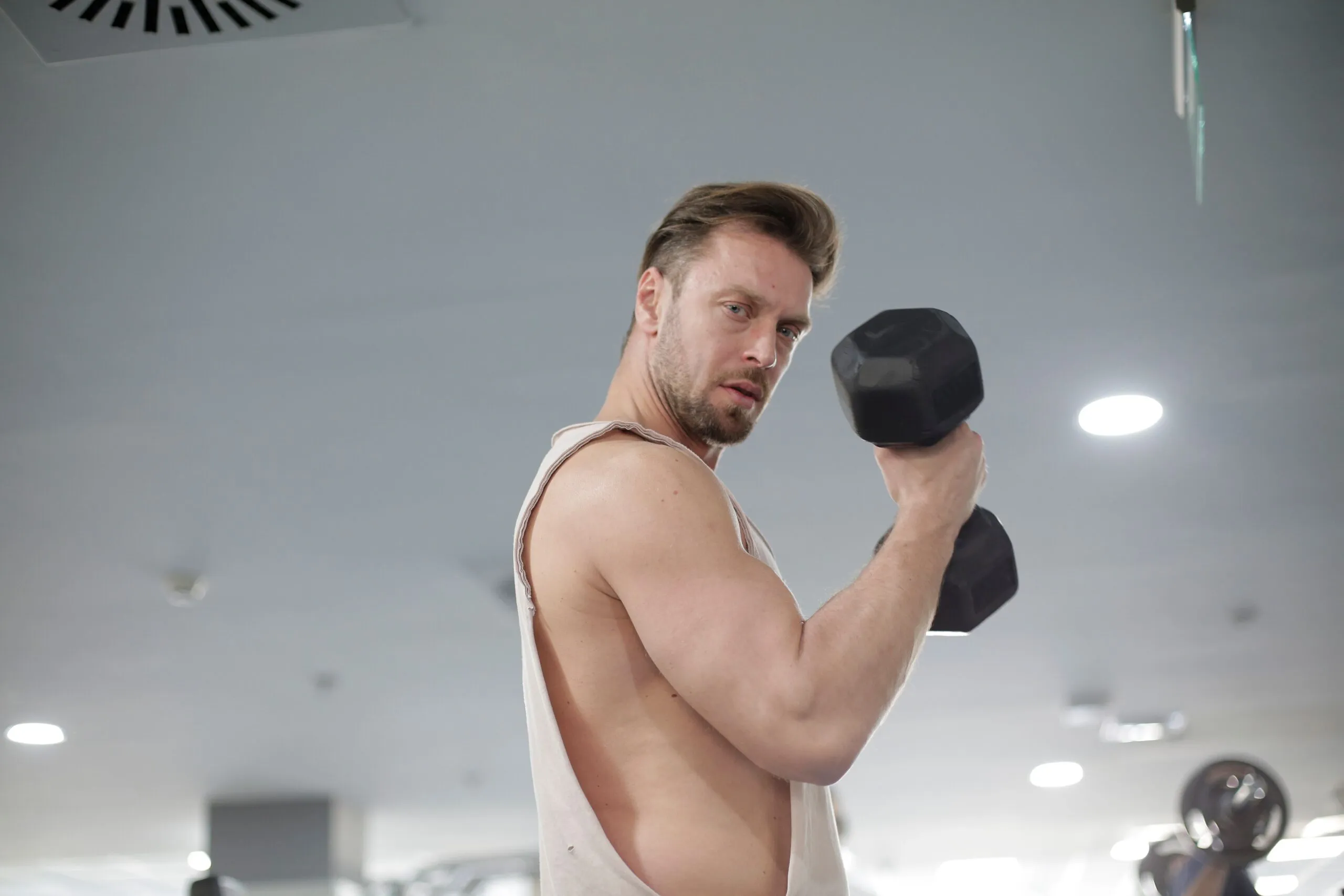 Strong man lifting dumbbell in gym, focused on bodybuilding and fitness.