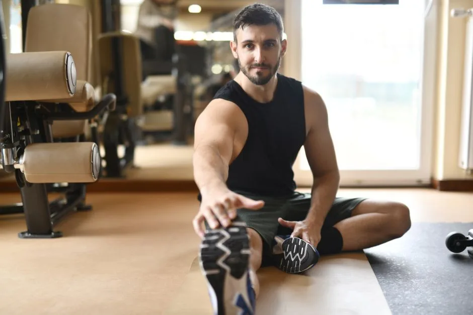 A man in gym clothes stretches on the floor in a modern fitness center.