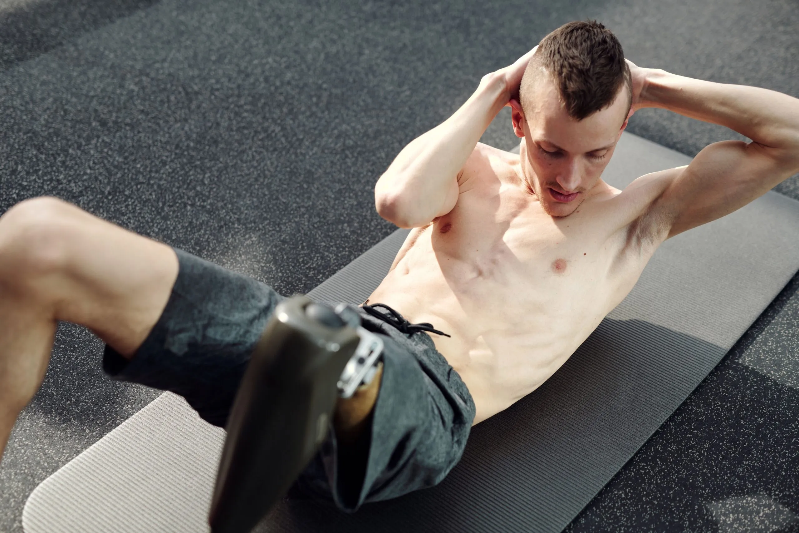 A determined man with a prosthetic leg doing sit-ups on a yoga mat indoors, showcasing strength and resilience.