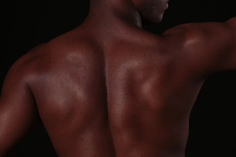 Close-up of a muscular man's back, showcasing defined skin and muscles in a studio setting.