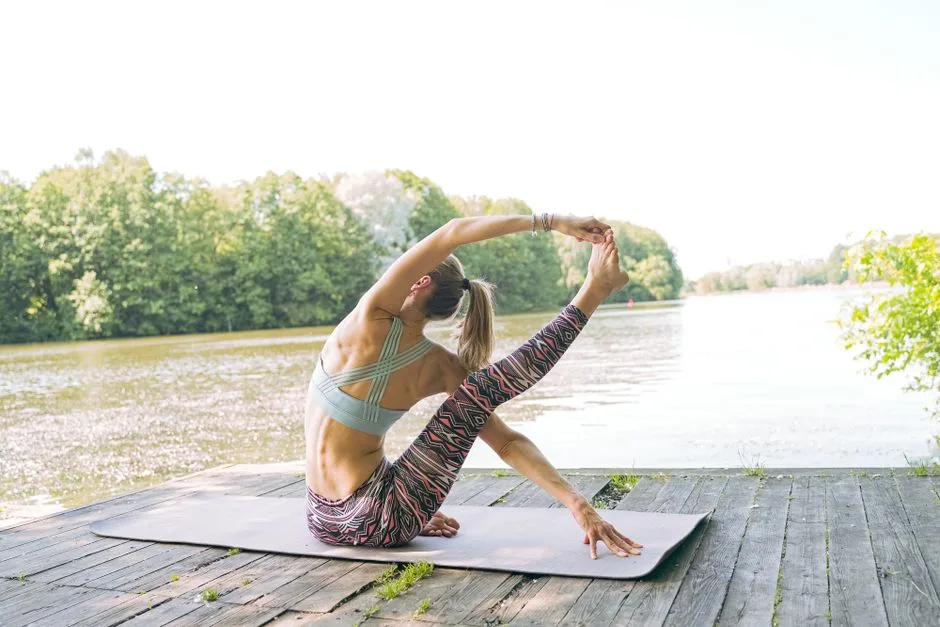 Woman practicing yoga on a dock by the lake, stretching with perfect form under a clear sky.