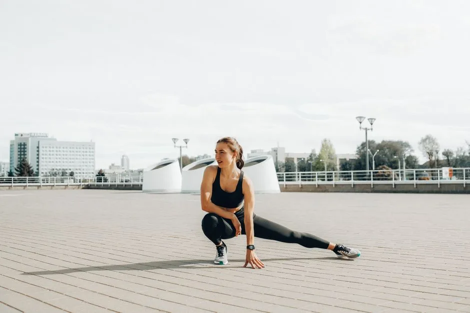 Young woman in black sportswear stretching outdoors in a sunny urban environment.