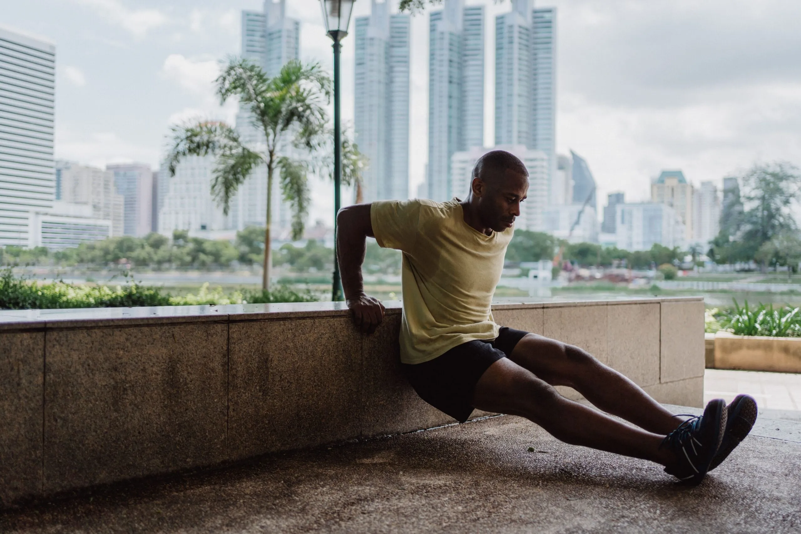 African American man doing tricep dips outdoors in a city park, emphasizing fitness and urban lifestyle.
