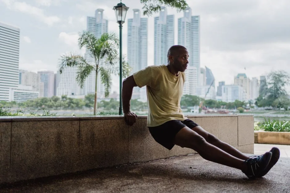 A man doing tricep dips on a park bench in an urban setting with skyscrapers in the background.