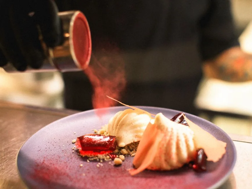 Close-up of a chef adding red powder to an elegant dessert on a blue plate.
