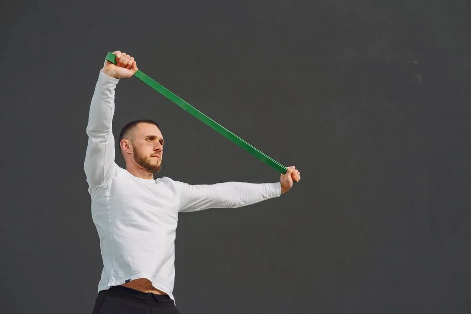 A man exercises with a resistance band against a plain background, promoting fitness.