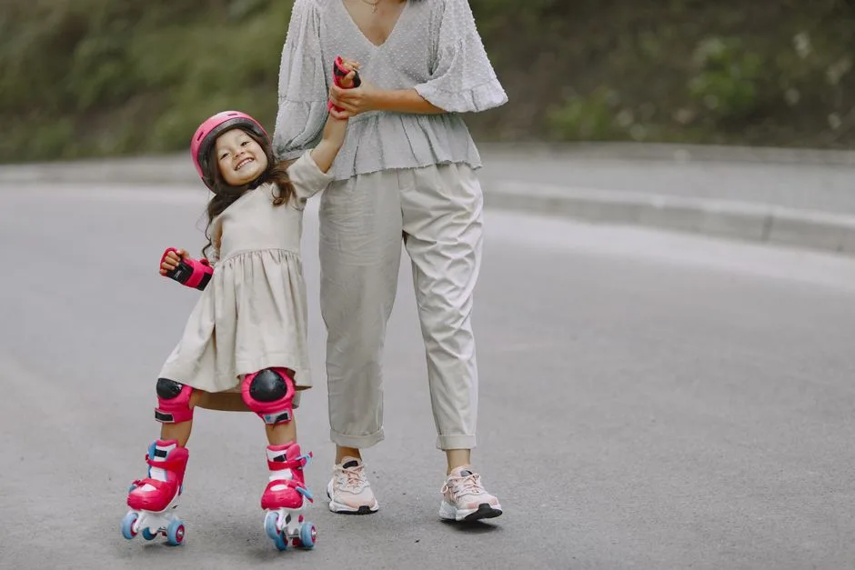 A mother helps her daughter learn rollerblading on an outdoor road, showcasing family bonding and teaching moments.