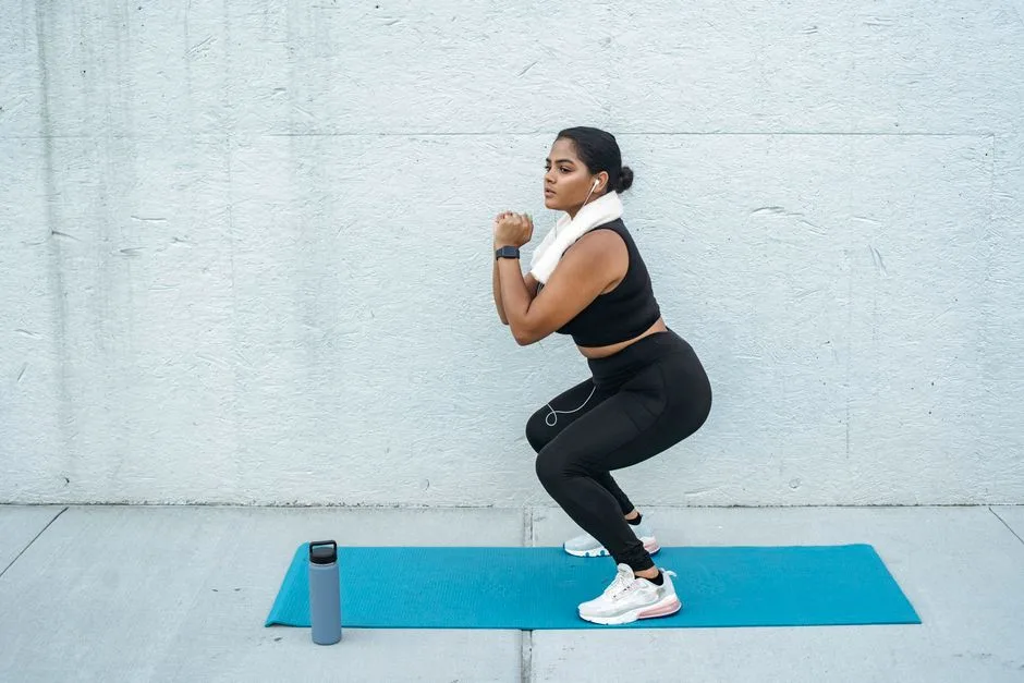 Confident woman doing squats on a yoga mat with a water bottle nearby. Fitness and lifestyle concept.