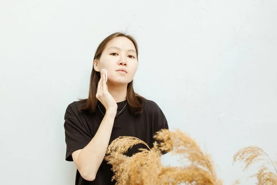 An Asian woman gently applies facial care in a calm, minimalist setting.