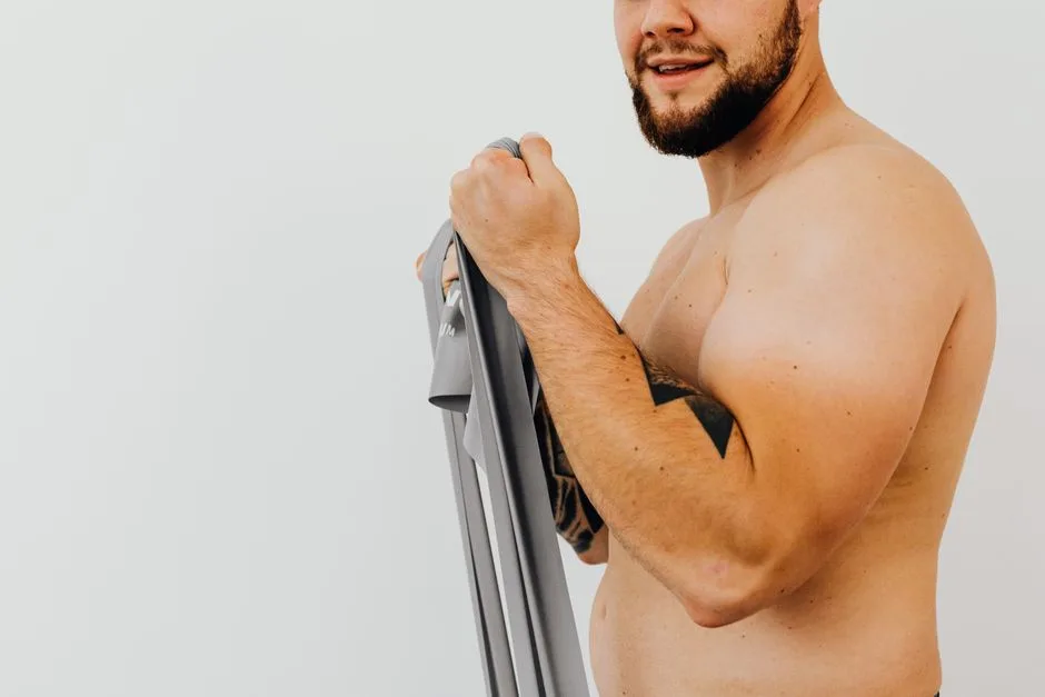 Shirtless man using resistance band for strength training indoors.