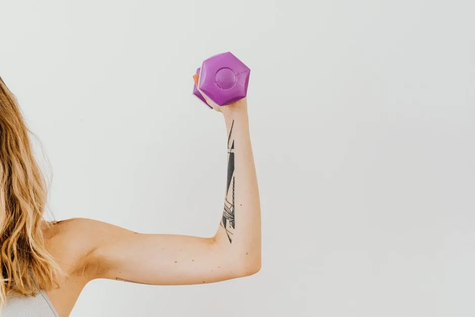 Close-up of a woman's tattooed arm lifting a purple dumbbell in a studio setting.