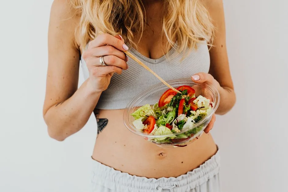 Woman in sports attire enjoys a fresh, nutritious salad, embodying a healthy lifestyle.