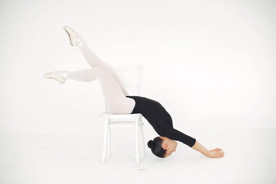 Ballet dancer gracefully stretching on a chair in a studio setting.