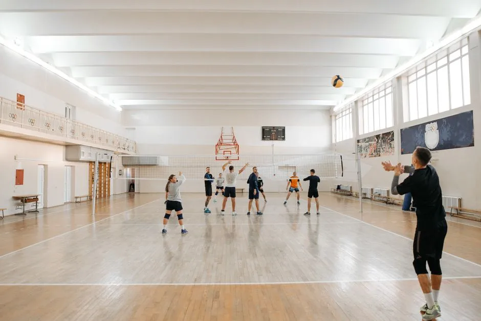 Adults energetically practicing volleyball indoors with a focus on teamwork.