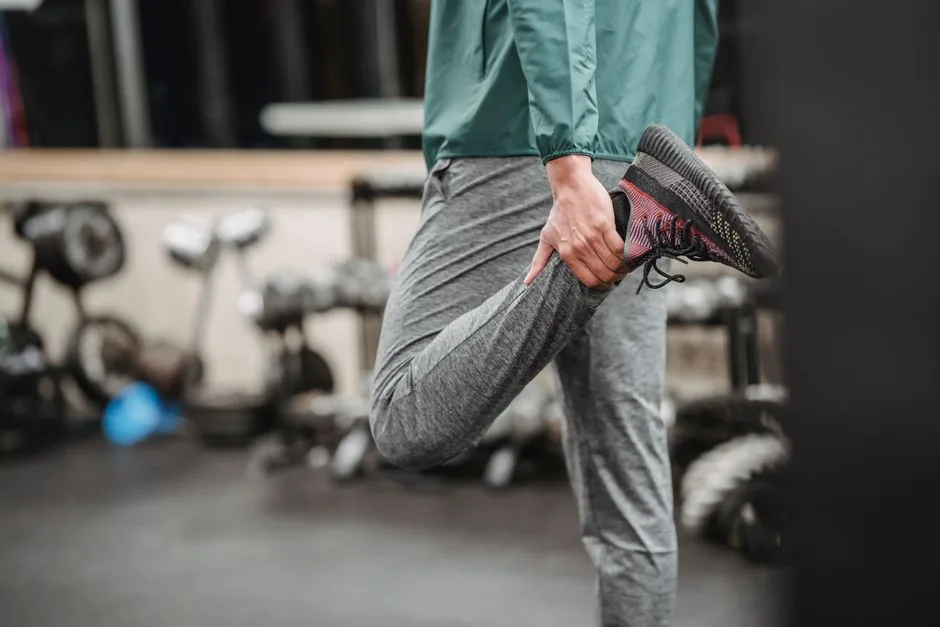 Crop anonymous male in sportswear warming up while stretching legs on blurred background of sport club with gym equipment