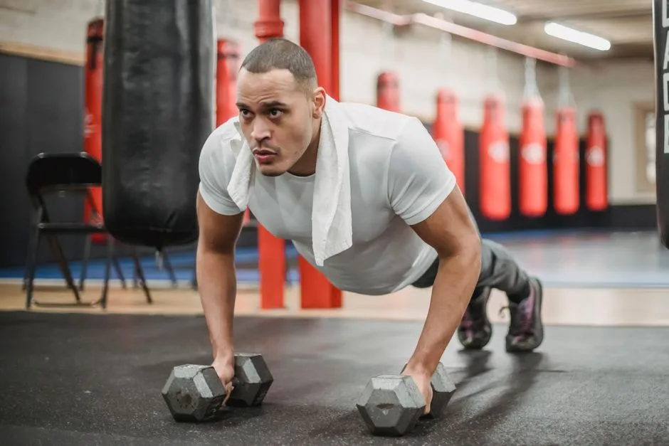 Full body powerful focused ethnic sportsman in activewear doing push up exercises with dumbbells during intense workout in contemporary gym