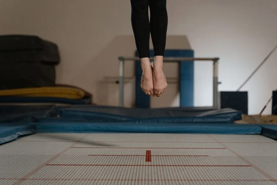 Athlete jumping on trampoline indoors, captured mid-air with focus on legs.
