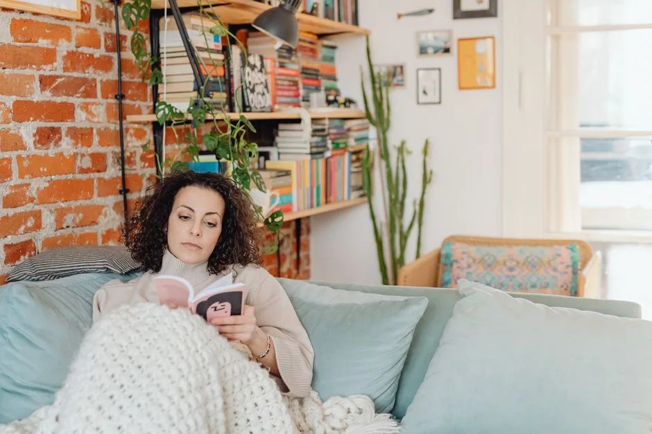 Woman relaxing with a book on a cozy sofa in a home library setting.